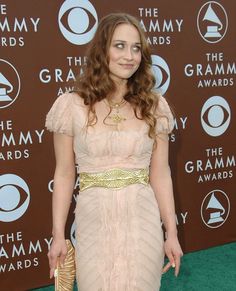 a woman in a pink dress and gold purse at an awards event with her hand on her hip