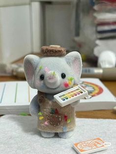 a small toy elephant holding a paintbrush on top of a table next to a remote control