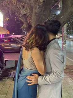 a man and woman standing next to each other in front of a tree at night