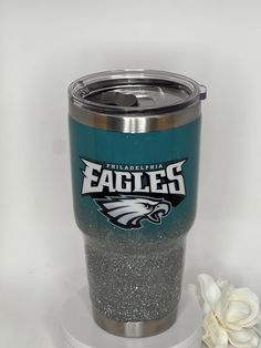 the philadelphia eagles glitter tumbler cup is next to a flower on a white background