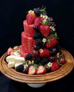 a cake made out of fruit and cheese on top of a wooden platter with flowers