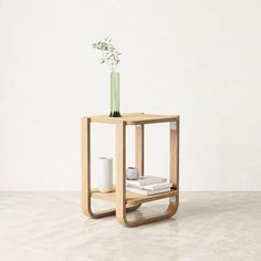 a small wooden table with a vase on top and books in the bottom, next to it