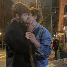 two young men embracing each other on the street at night time with people in the background