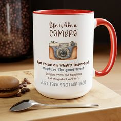 a red and white coffee mug sitting on top of a wooden table next to a spoon