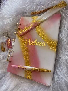 a pink and white notebook with gold glitters on it next to a keychain