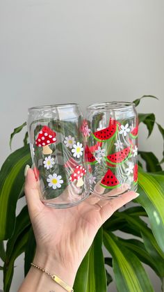 a person holding up two glasses with watermelon designs on them and daisies