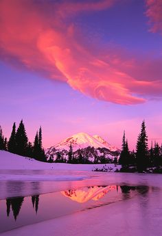 a snow covered mountain is reflected in the still water at sunset with pink and purple clouds