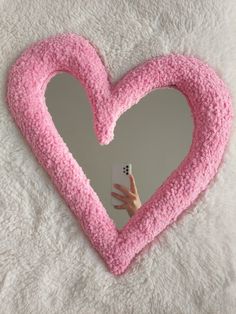 a pink heart shaped pillow holding a cell phone