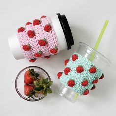 two cups with strawberries on them next to a strawberry covered drink sleeve and cup holder