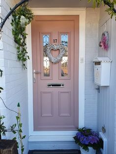 a pink front door with two wreaths on the side and flowers in pots next to it