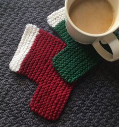 two knitted mitts sitting next to a cup of coffee