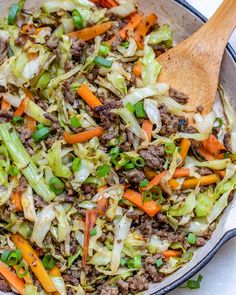 a skillet filled with ground beef, carrots and celery next to a wooden spoon