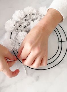 two hands are working on the wire and fabric wreath with cotton pom - poms