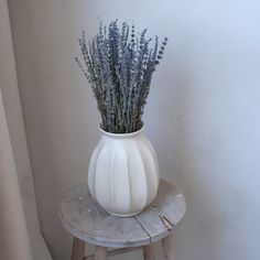 a white vase filled with lavender on top of a wooden stool next to a window