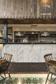 the interior of a restaurant with wooden tables and chairs in front of an open kitchen