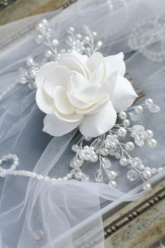 a white flower and some pearls on a piece of organe net with beading