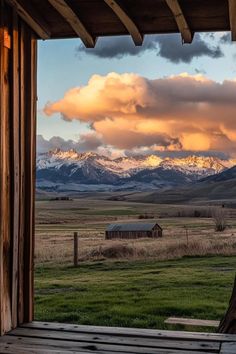 the mountains are covered in clouds as seen from an open cabin door with a bench