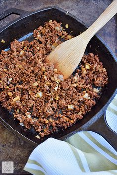 a skillet filled with ground beef and onions on top of a towel next to a wooden spoon