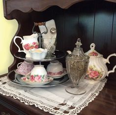 a table topped with plates and cups on top of a wooden dresser next to a vase