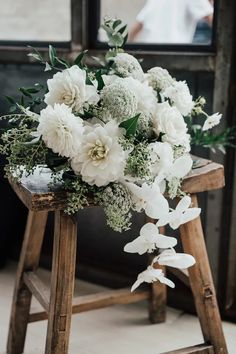 a bouquet of white flowers sitting on top of a wooden stool next to a window