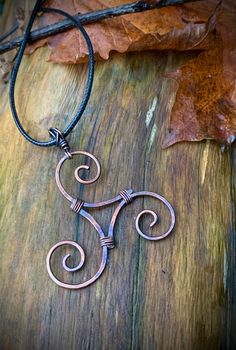 a metal pendant on a wooden surface with leaves in the background and a leaf laying next to it