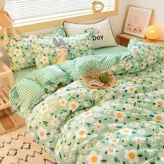 a bed with green and white flowers on it, next to a night stand in front of a window