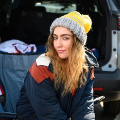 a woman sitting in the back of a van wearing a knitted hat and jacket