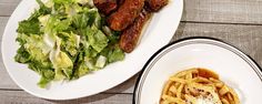 two plates of food on a table next to a bowl of salad and chicken wings