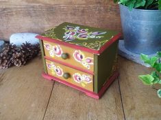 a painted wooden box sitting on top of a wooden floor next to a potted plant