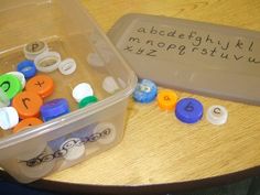 a plastic container filled with lots of different colored buttons next to a plastic box that has letters on it