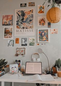 a white desk topped with a laptop computer next to a wall covered in pictures and plants