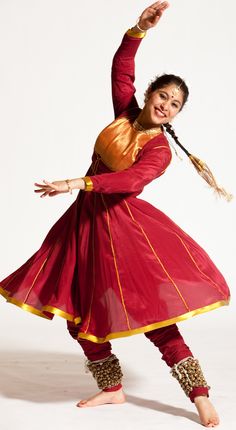 a woman in a red and gold dress is dancing with her arms out to the side