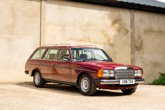 an old red station wagon is parked in front of a concrete wall and green shrubbery