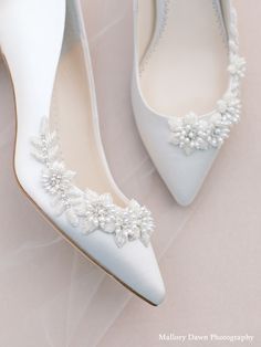 a pair of white wedding shoes with pearls on the toe and heels are sitting next to each other