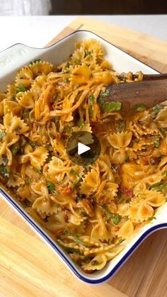 a bowl filled with pasta and vegetables on top of a wooden table next to a cutting board