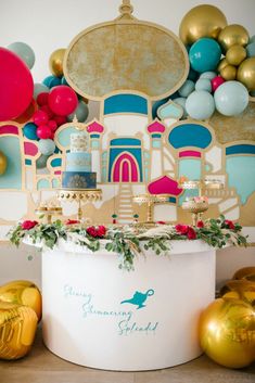 a table topped with cake and balloons in front of a wall filled with colorful balloons