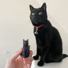 a black cat sitting on top of a table next to a small figurine