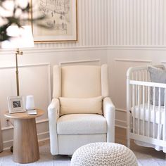 a baby's room with a white chair, crib and small round ottoman