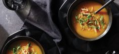 two bowls filled with soup on top of a black table next to silver spoons