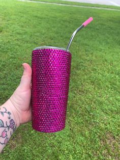 a hand holding a purple cup with a toothbrush in it on the grass outside