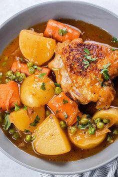 a white bowl filled with chicken, potatoes and carrots on top of a table