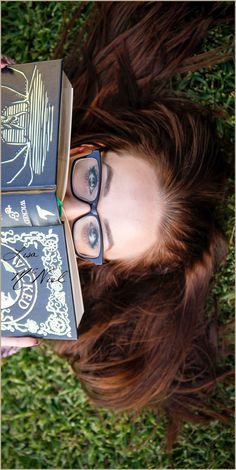 a woman with glasses is laying on the grass and holding two books in her hands