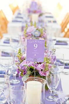 the table is set with purple and white flowers, candles, and place cards on it