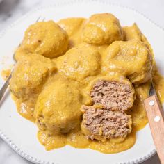 a white plate topped with meatballs covered in gravy next to a knife and fork