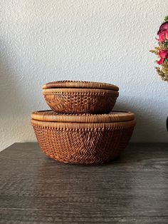 three wicker bowls sitting on top of a wooden table next to a vase with flowers