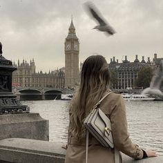 a woman sitting on a wall looking at the water with a clock tower in the background