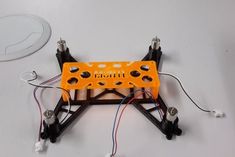 an orange and black robot with wires attached to it's back end on a white surface