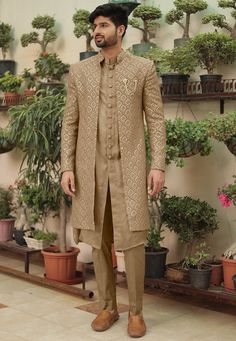 a man standing in front of potted plants wearing a tan sherve and brown pants