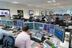 two men are sitting in front of multiple monitors