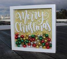 a merry christmas card with ornaments in the frame on top of a wooden table next to a cityscape